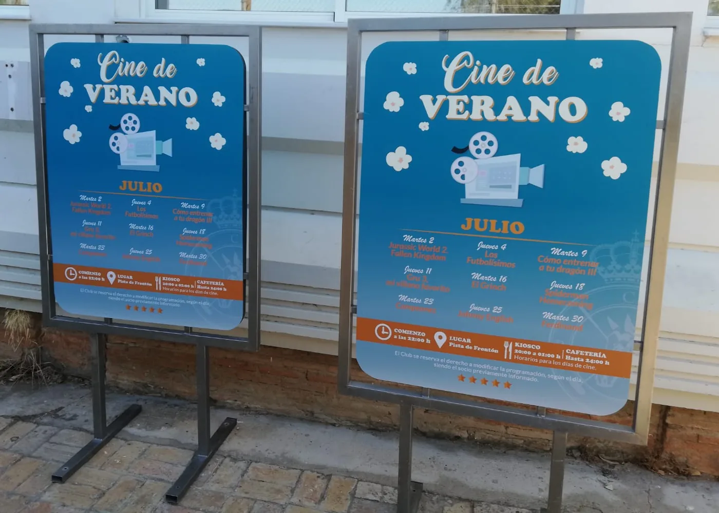 Dos carteles impresos con la programación mensual de cine de verano en expositores de pie