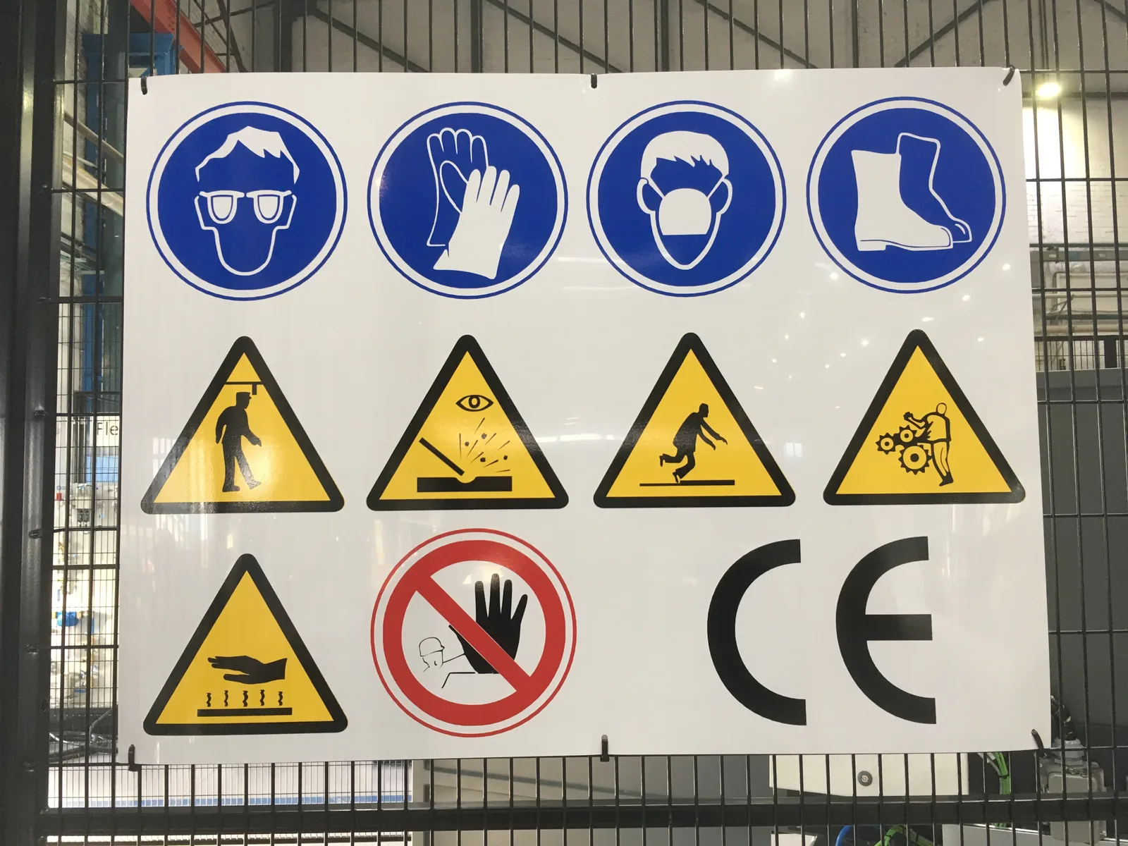 Cartel de señalización de seguridad con pictogramas de protección individual instalado en un vallado industrial