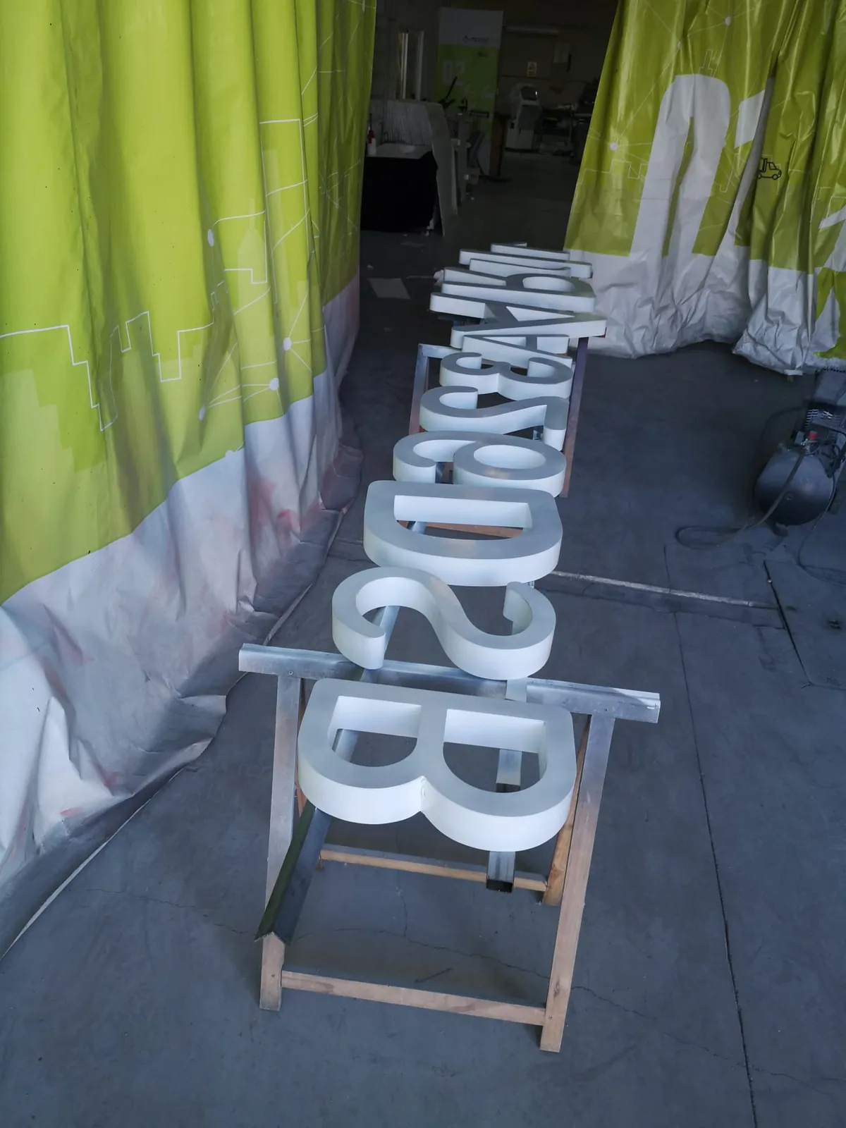 Fila de letras corpóreas recién pintadas en blanco, apoyadas sobre caballetes en la zona de pintura del taller