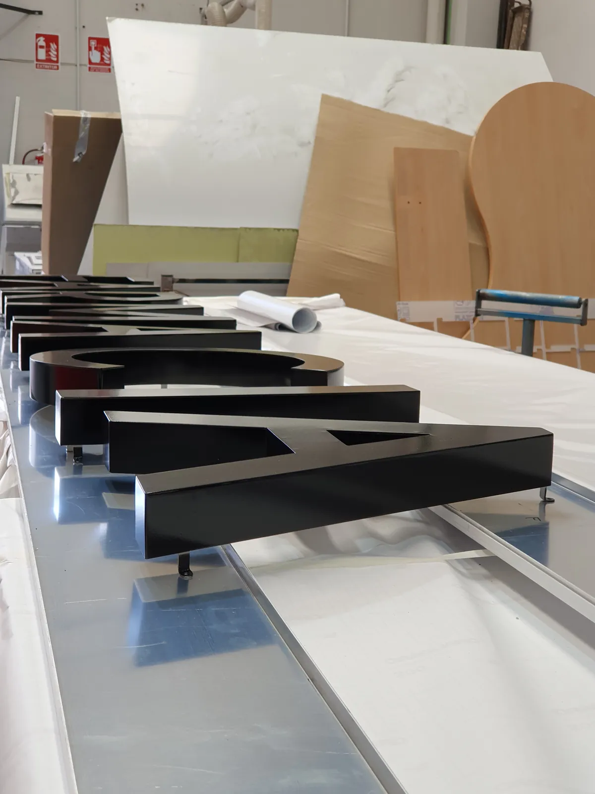 Letras corpóreas de aluminio lacado en negro brillante con espárragos de fijación, alineadas sobre una bandeja en el taller